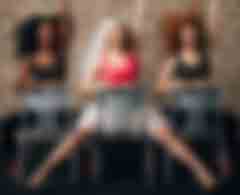 Trois danseuses de chair dance assises à califourchon sur leur chaise, un bras sur le dossier l'autre levé, en chorégraphie, dans une ambiance festive